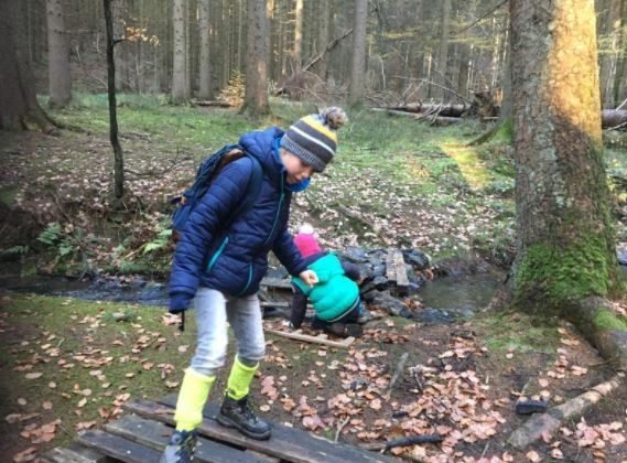 Een jongen en een meisje steken een houten brug over in het bos.