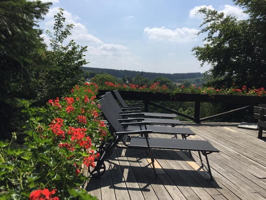 Een rij ligstoelen op een terras met rode bloemen op de achtergrond