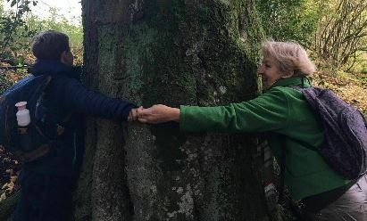 Twee mensen omhelzen een boom in het bos.