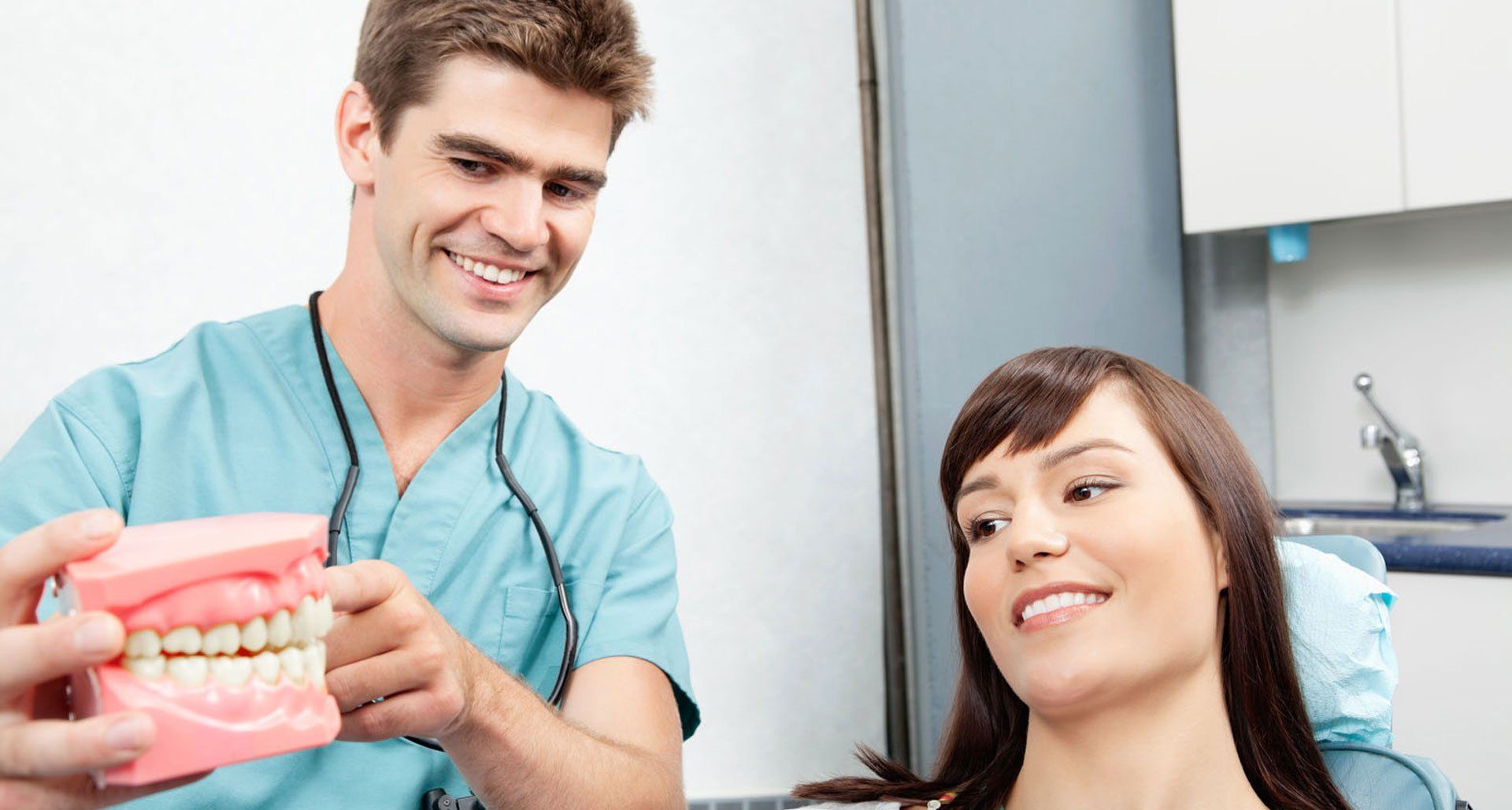 Dentist showing a patient a teeth model in an exam room; both smiling.
