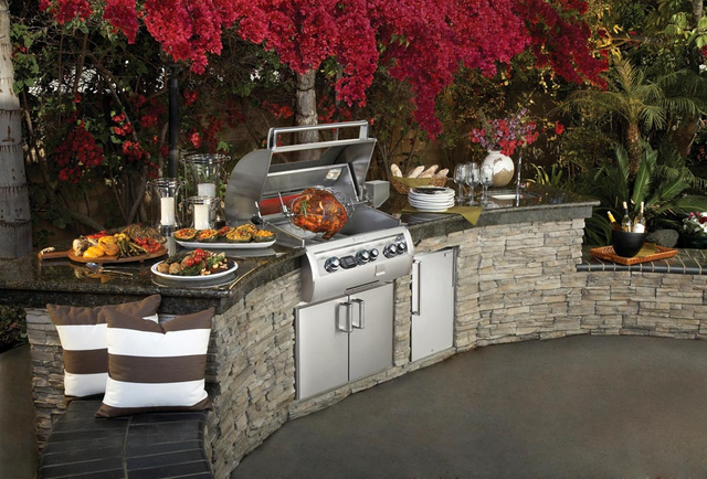 An outdoor kitchen with a grill and plates of food on the counter.