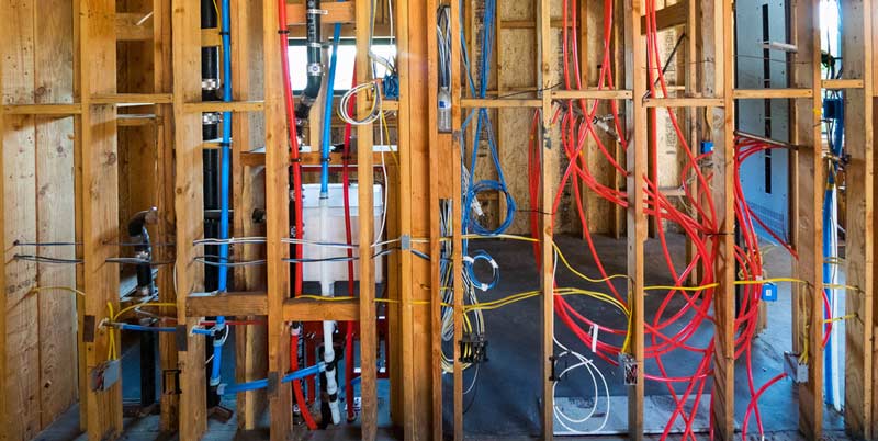 A room in a house under construction with pipes and wires.