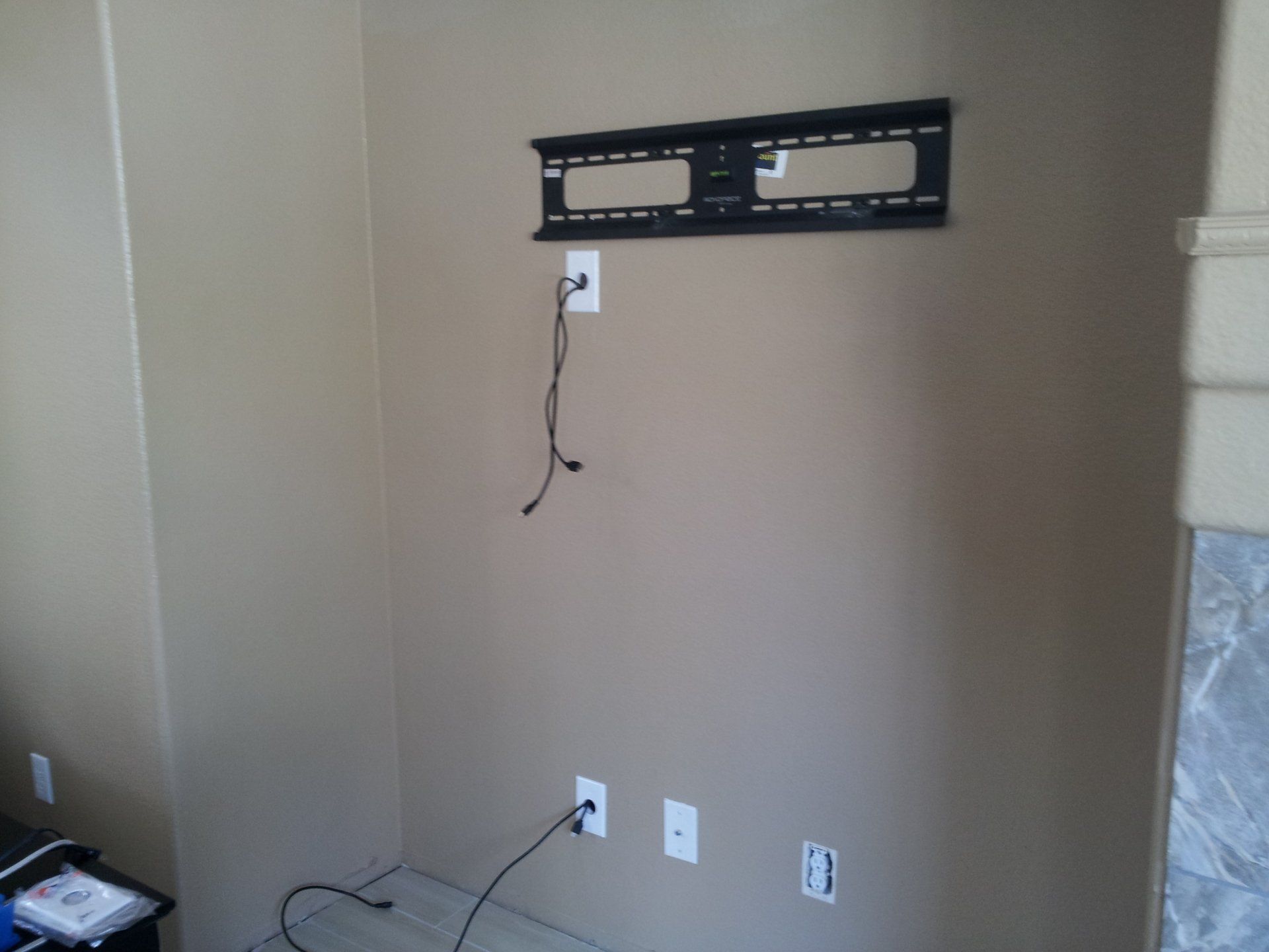 A tan wall with a mounted TV bracket, electrical outlets, and cords.