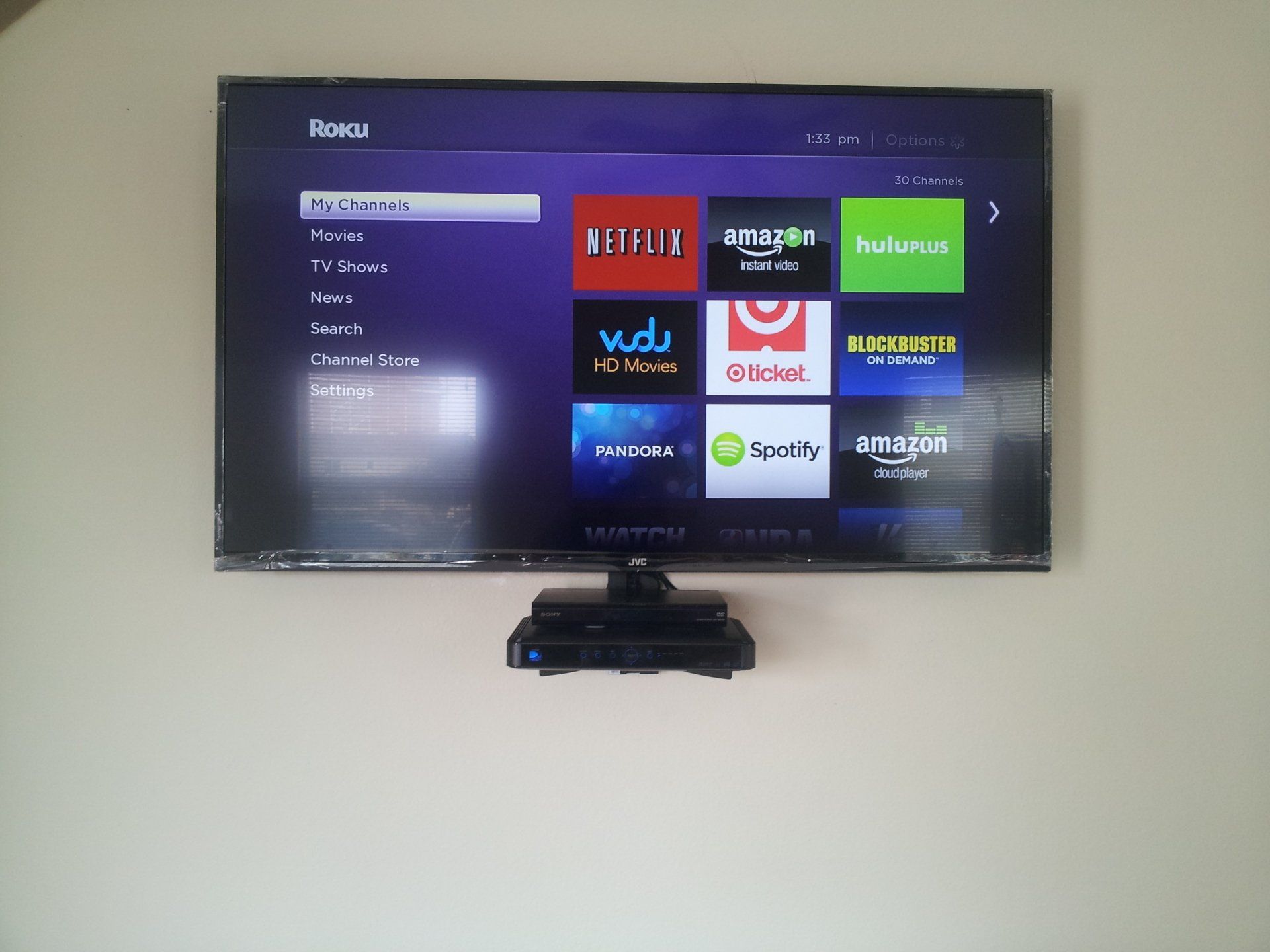 A wall-mounted TV displaying the Roku home screen, with a Roku streaming device below.