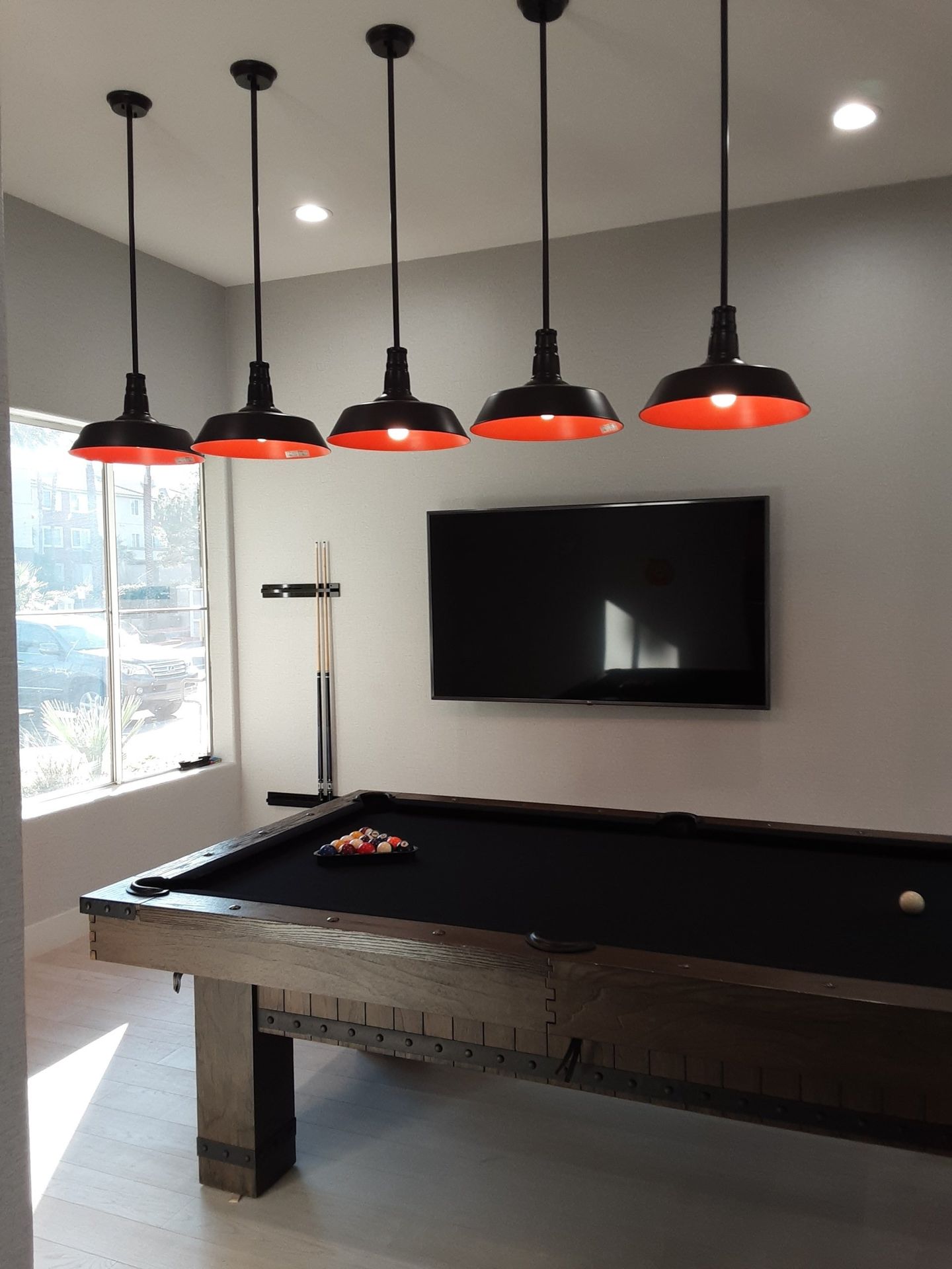 Pool table under five pendant lights in a room with a window and a wall-mounted television.
