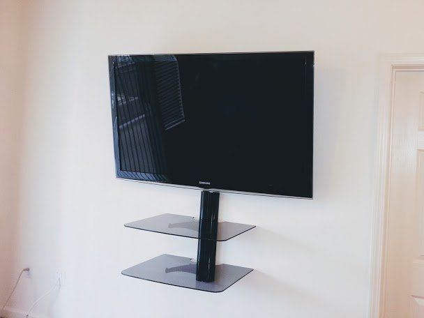 A flat-screen TV mounted on a white wall above two floating glass shelves.