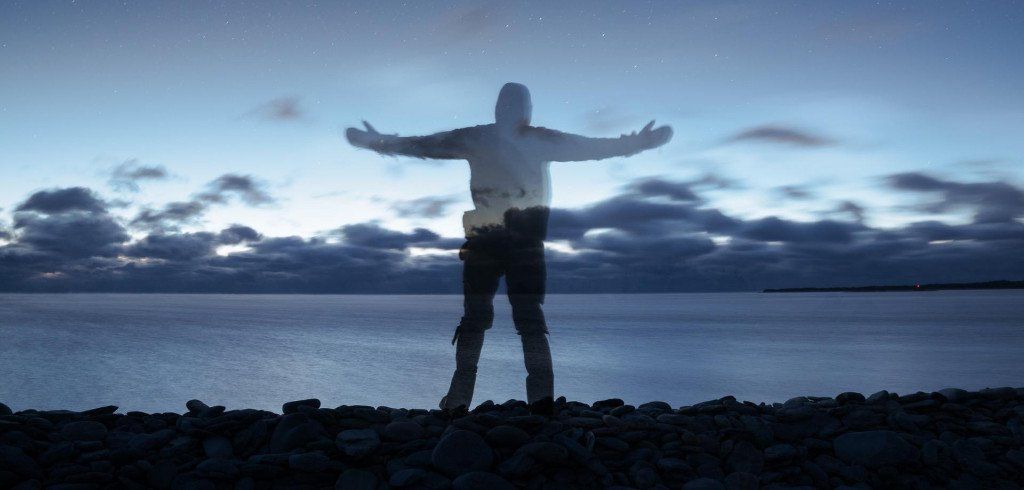 A silhouette of a man standing on a beach with his arms outstretched.