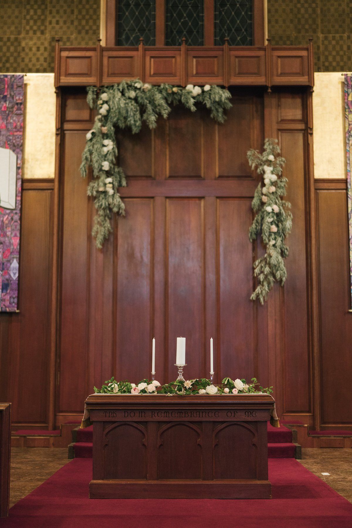 Wooden altar decorated with flowers and greenery in a church. Three candles stand on the altar.