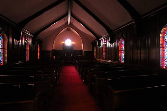 Interior of a church with dark wood paneling, stained glass windows, and a red carpet leading to a rounded window.