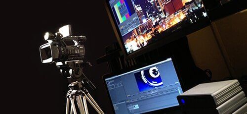 Video camera on tripod set up in front of a monitor displaying video editing software, recording studio.