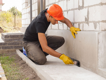 Man providing basement services by waterproofing basement from outside of home