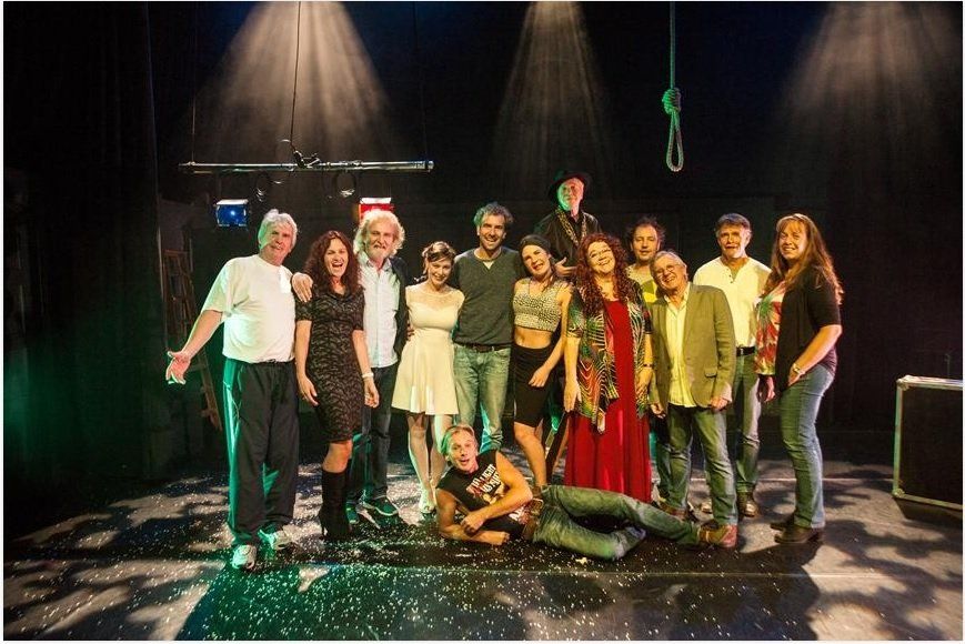 Amateurs! Een groep artiesten poseert op een podium, sommigen glimlachen, met podiumverlichting en een strop.