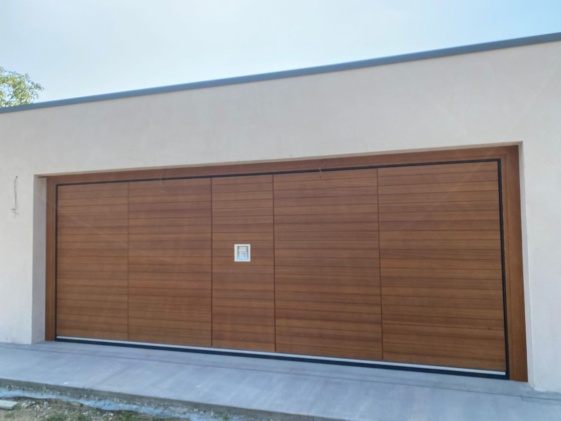 Un'ampia e moderna porta da garage orizzontale con finitura effetto legno chiaro, incastonata in una semplice parete esterna bianca.