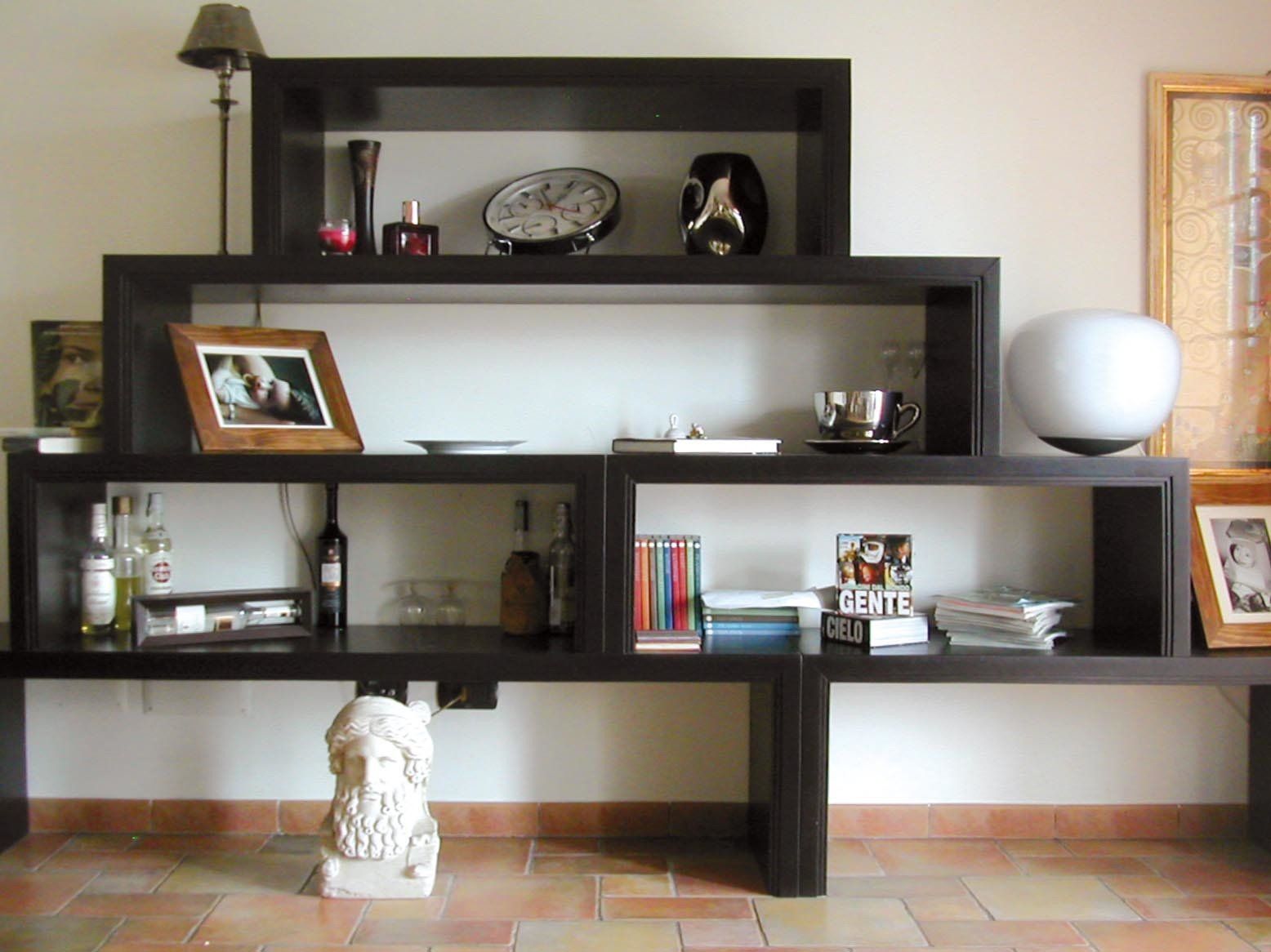 Scaffale a gradini marrone scuro con vari oggetti decorativi contro una parete bianca.