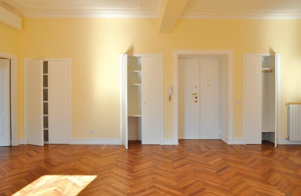 Stanza vuota con pavimento in parquet, pareti gialle e armadi bianchi a muro.