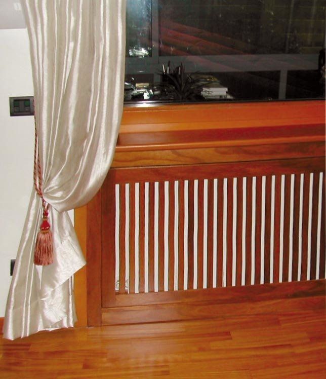 Tenda color crema legata con una nappa, vicino a un copritermosifone in legno con listelli bianchi verticali e a una finestra.