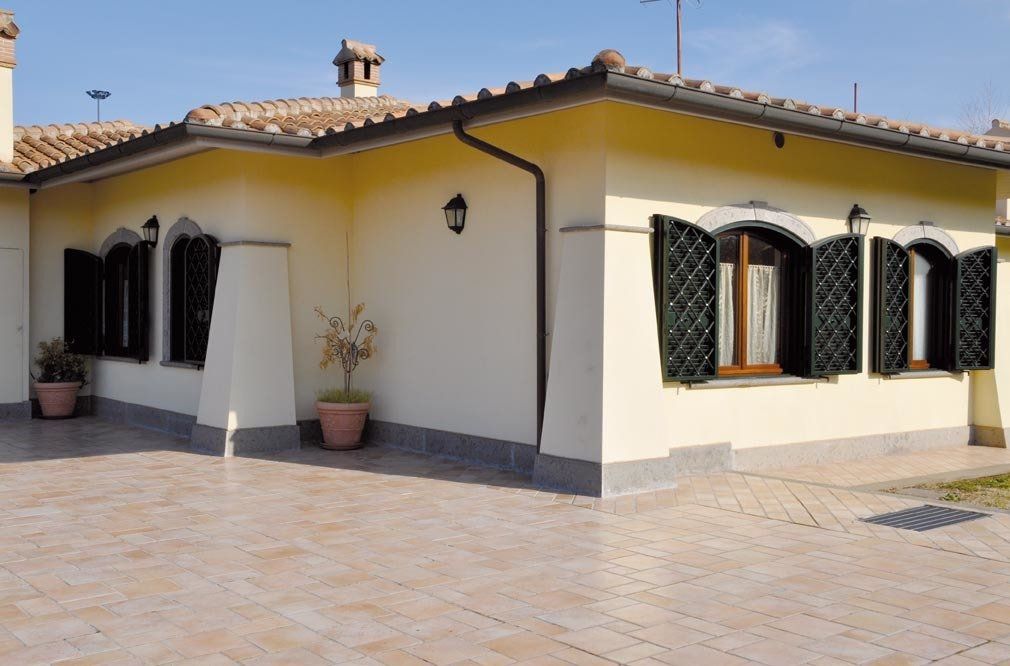 Casa in stucco giallo con persiane nere e patio piastrellato in terracotta.