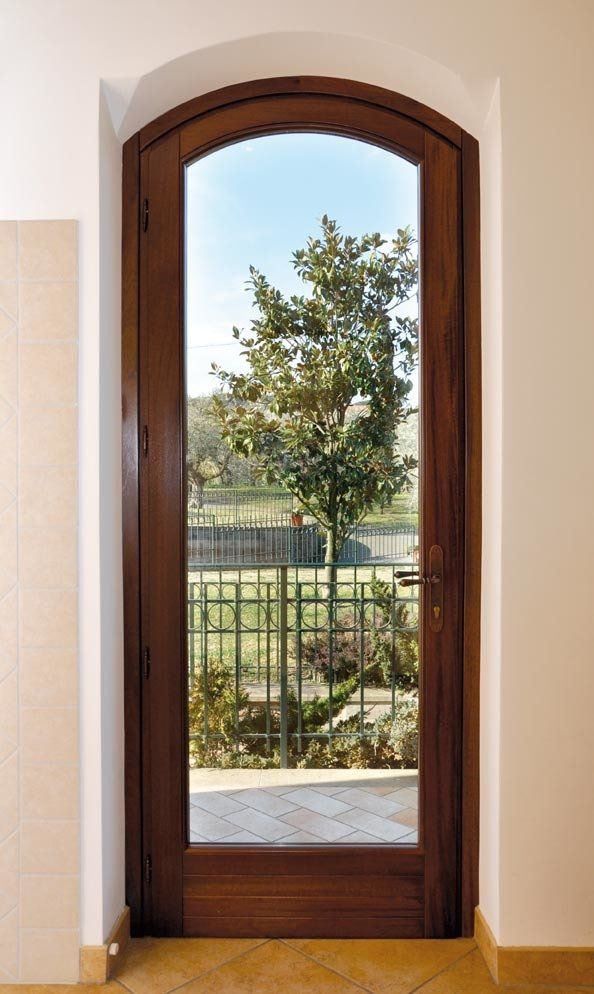 Porta ad arco in legno con vetro trasparente, che rivela un albero e una ringhiera in ferro battuto all'esterno.