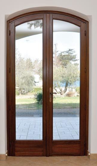 Doppie porte ad arco in legno con pannelli in vetro, che rivelano un cortile con alberi e un patio piastrellato.