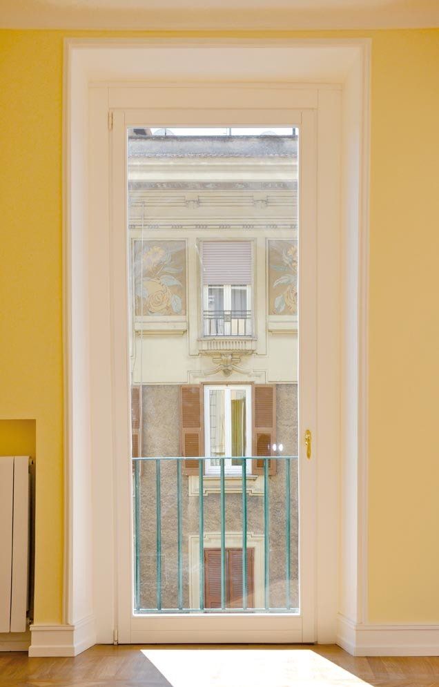 Porta bianca con vista su un altro edificio, ringhiera verde e pareti gialle.