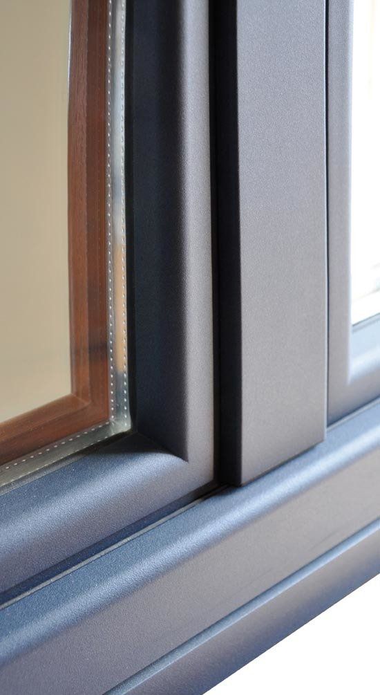 Primo piano del telaio di una finestra con interno in legno marrone ed esterno grigio scuro, in un ambiente moderno.