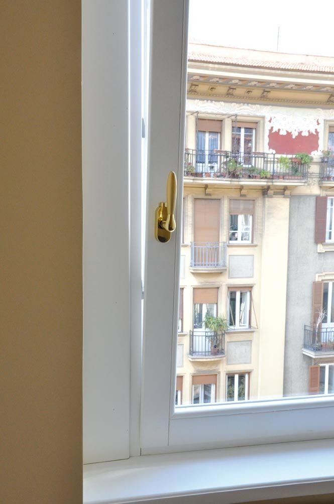 Finestra bianca aperta con maniglia dorata, che mostra un condominio dall'altra parte della strada.
