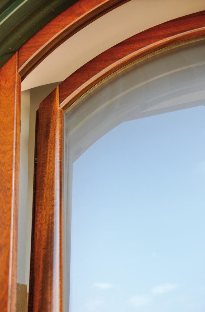 Telaio della finestra in legno con parte superiore arcuata, cielo azzurro visibile.