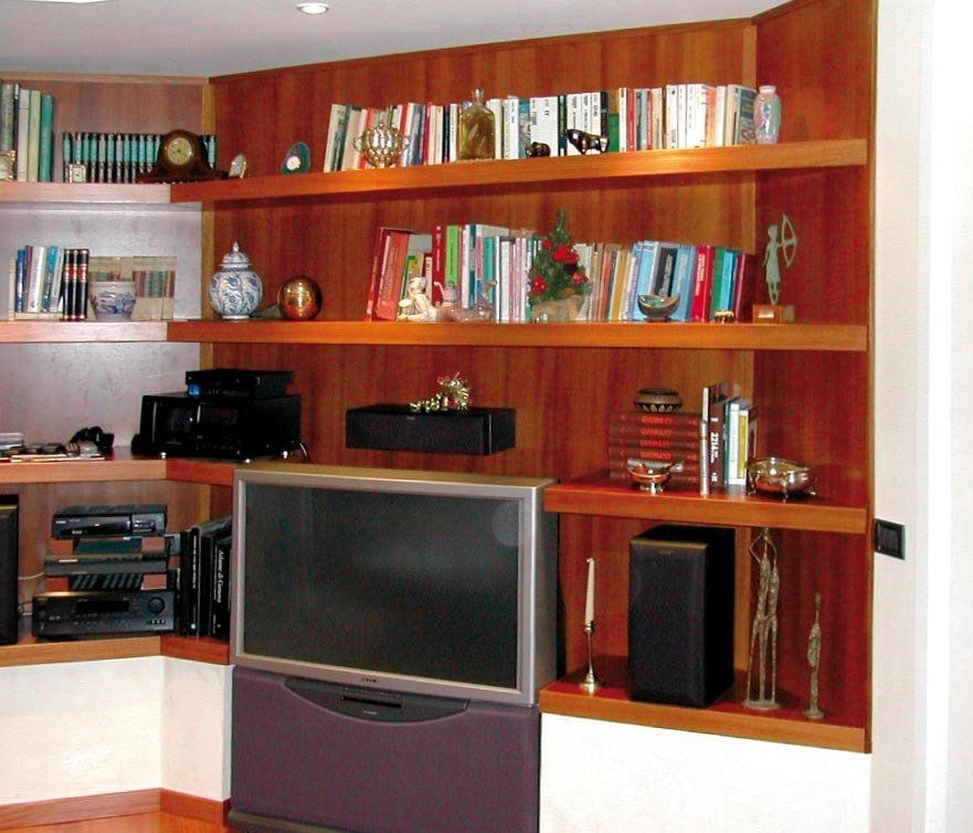 Scaffali in legno integrati con libri, oggetti decorativi e apparecchiature multimediali, tra cui TV e altoparlanti.