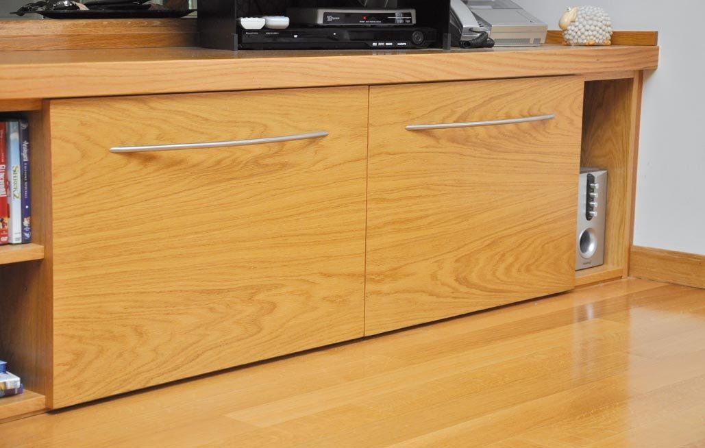 Mobiletto porta TV in legno con ante chiuse e maniglie metalliche, su pavimento in legno.