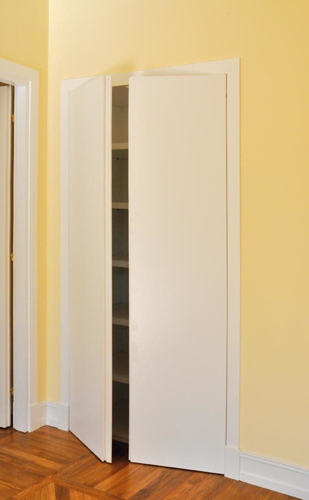 Le porte bianche a soffietto si aprono leggermente, rivelando gli scaffali all'interno di un armadio, situato in una stanza con pareti gialle e pavimento in legno.