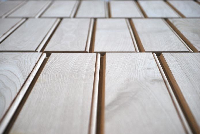 Pannelli in legno chiaro con scanalature verticali, disposti in file, pronti per l'installazione.