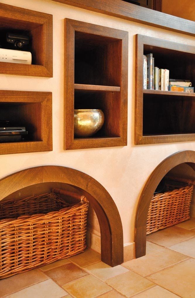Scaffali in legno a muro con aperture ad arco contenenti cesti di vimini. Vernice marrone chiaro e piastrelle.