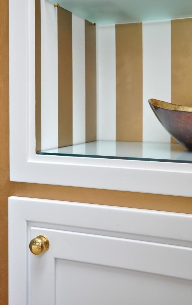 Mobiletto bianco a muro con ripiano in vetro, interno a righe bianche e dorate e ciotola decorativa.