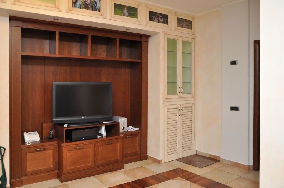 Mobile TV in legno con TV, scaffali e armadietti in una stanza con pareti e pavimento chiari.
