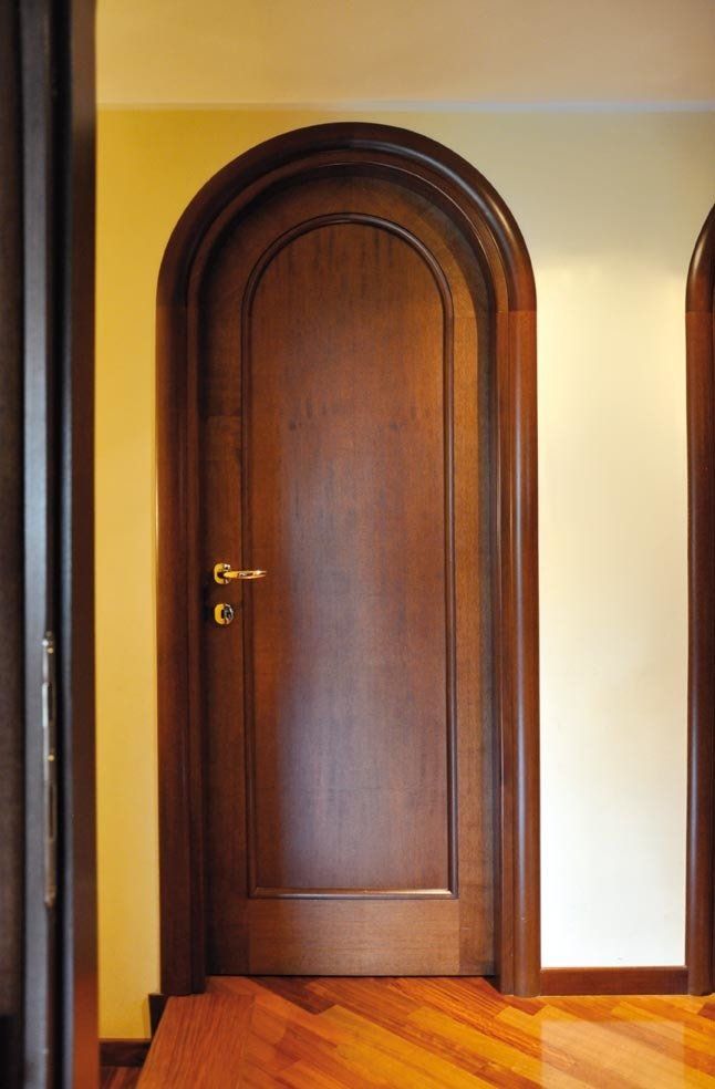 Porta ad arco in legno su un portone, con maniglia dorata e caldo pavimento in legno.