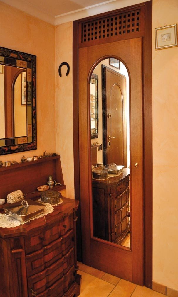 Porta a specchio con cornice in legno, con un mobiletto decorativo in legno e uno specchio da parete sulla sinistra.