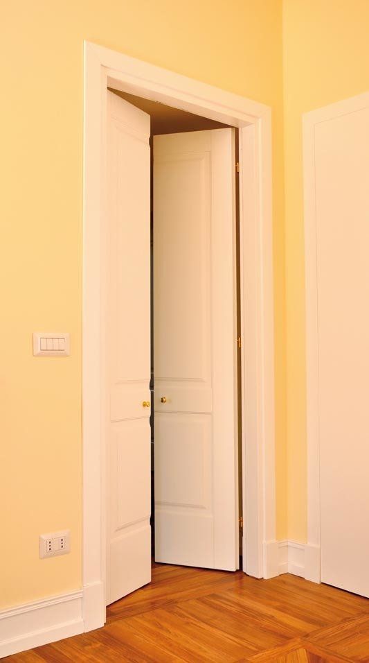 Porta interna bianca socchiusa in una stanza con pareti giallo chiaro e pavimento in legno.