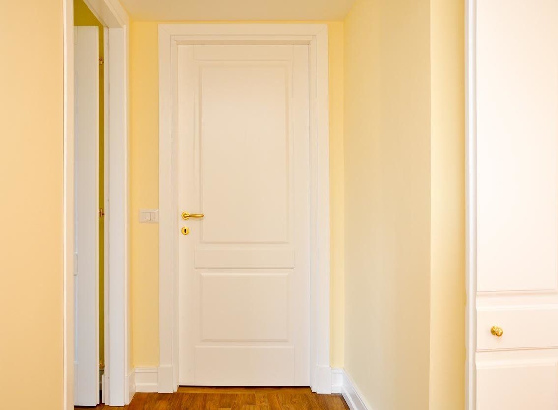 Porta bianca in un corridoio dalle pareti gialle. Un'altra porta visibile sulla sinistra, un mobiletto bianco sulla destra.
