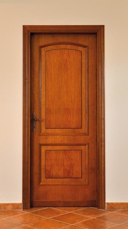 Porta in legno, marrone con pannelli, incastonata in una cornice contro una parete beige chiaro e un pavimento piastrellato.
