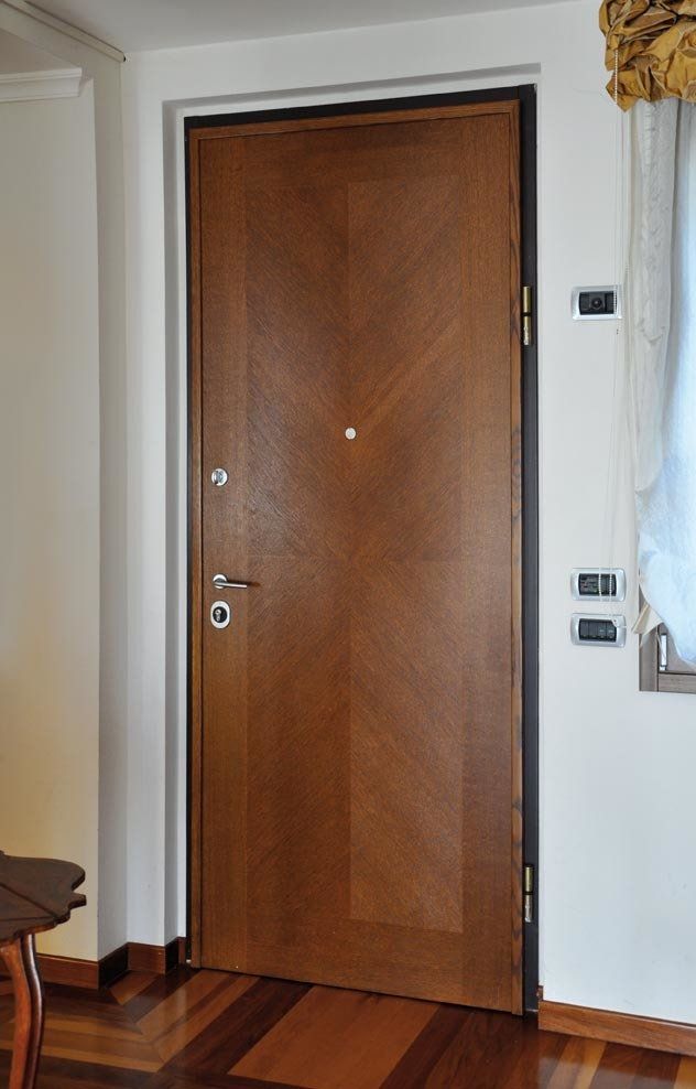 Porta in legno con venature diagonali, marrone, inserita in una parete bianca con finiture scure.