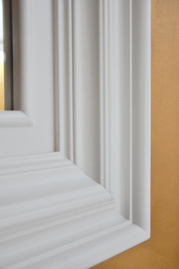 Cornice bianca della finestra con modanature dettagliate contro una parete gialla.