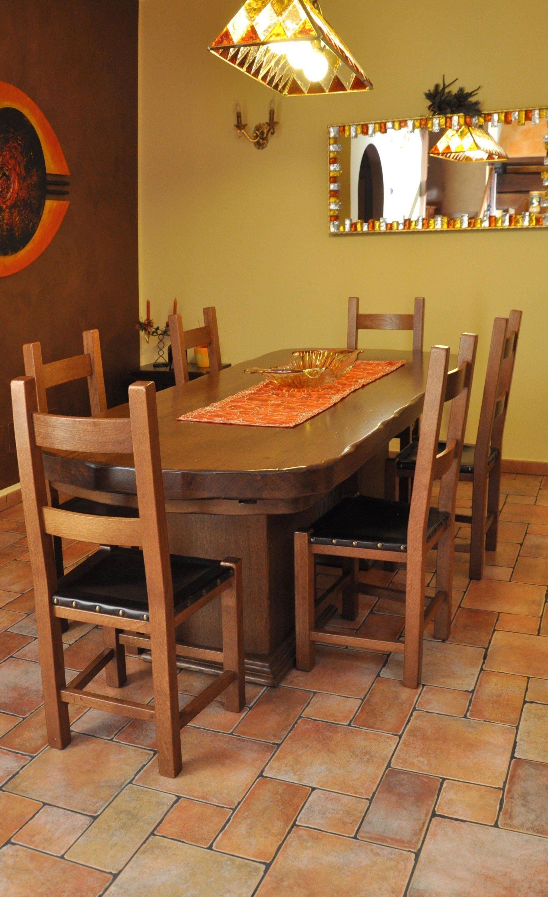 Sala da pranzo con tavolo e sedie in legno, tappeto arancione, lampadario, specchio e pavimento piastrellato.