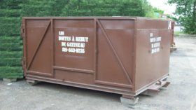 Brown metal container on a pallet, outdoors. Text on the side.