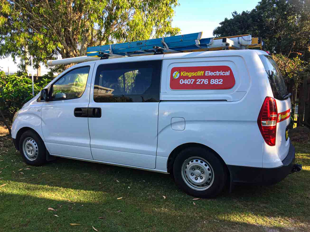 A white van with a ladder on top of it is parked in the grass.