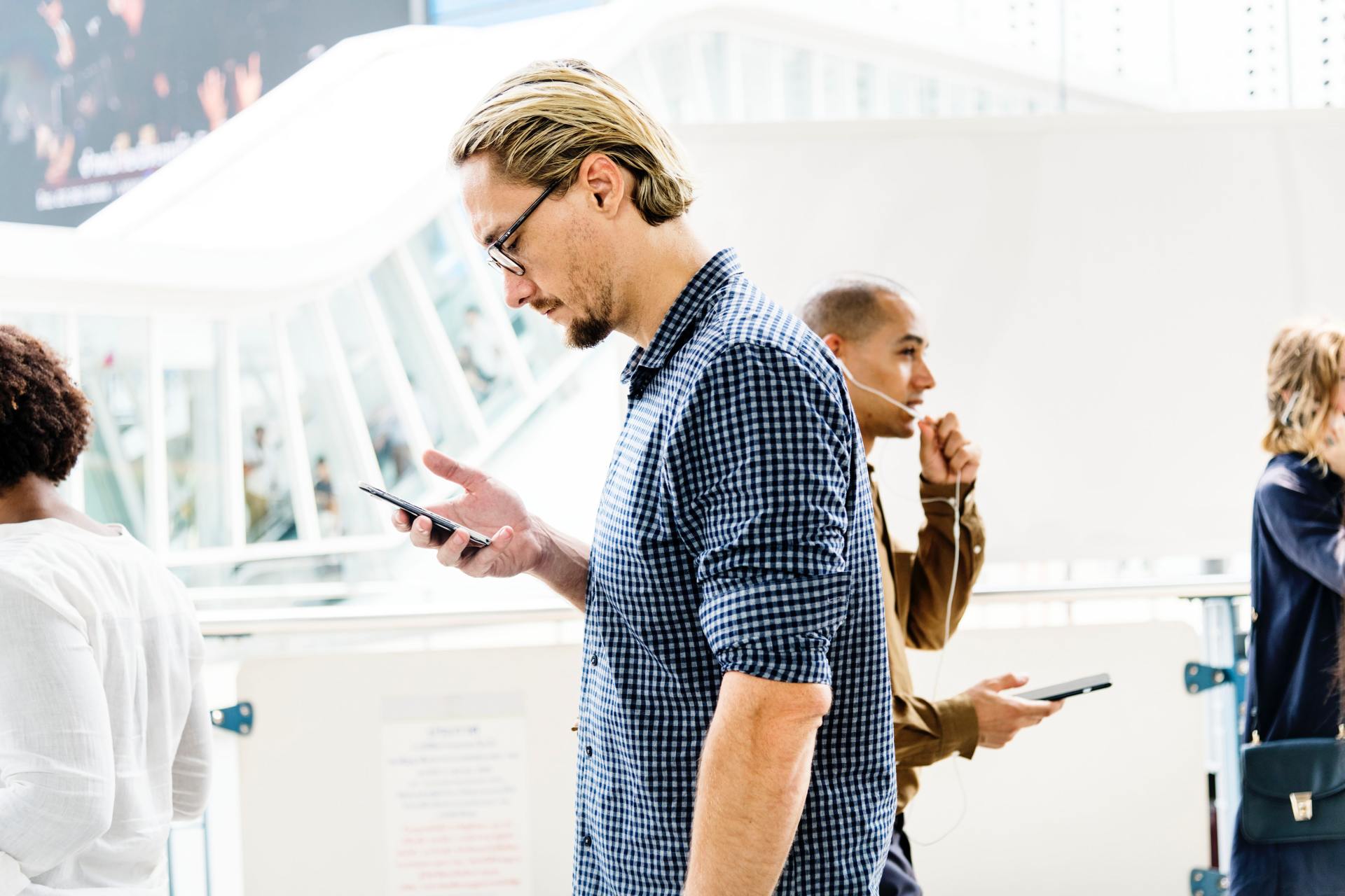 A man is looking at his cell phone while standing next to a group of people.