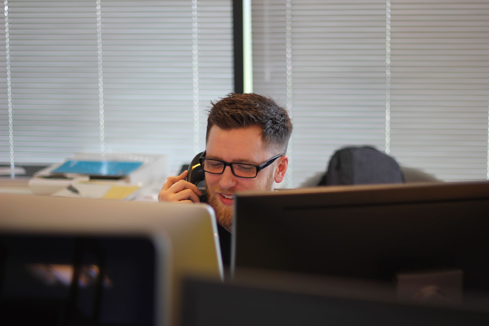A man is sitting in front of a computer talking on a cell phone.