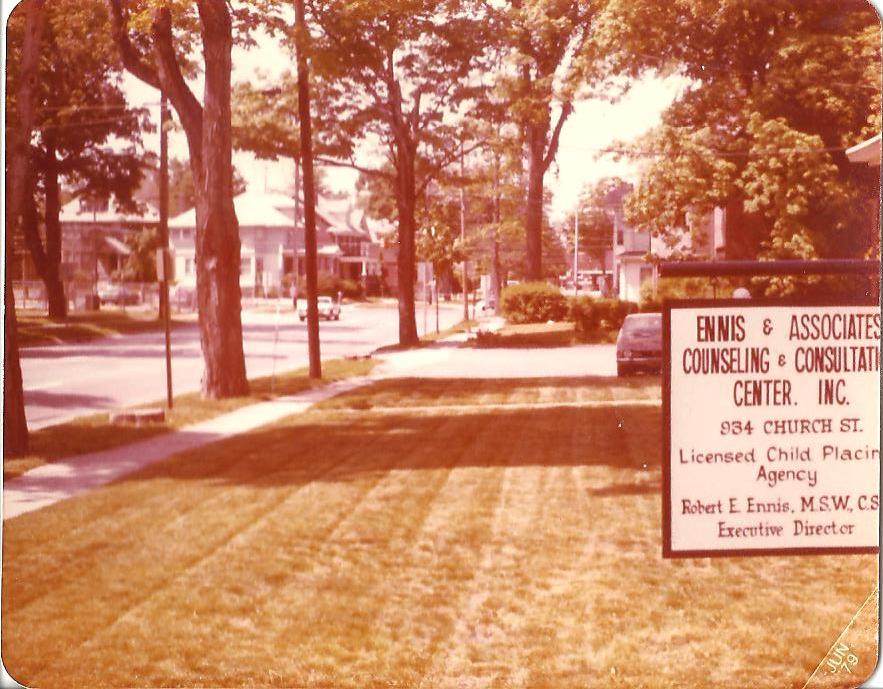 A sign for Ennis & Associates Counseling & Consulting Center on a lawn beside a residential street with mature trees.