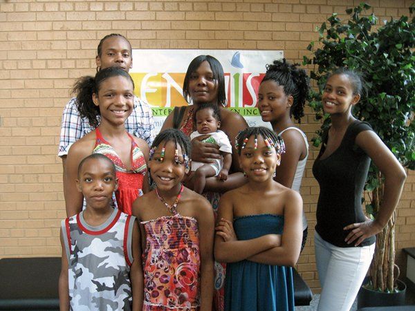 A group of ten people of various ages pose for a photo in front of a brick wall and a partial sign indoors.