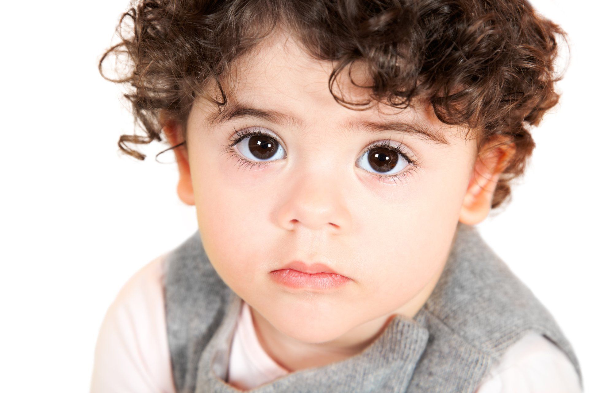A close-up portrait of a child with curly dark hair and large, dark eyes looking directly forward.