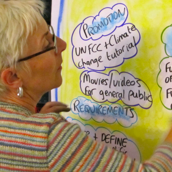 A person in a striped sweater writes on a yellow poster board with